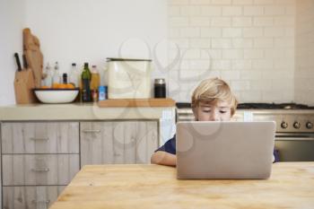 Young boy using laptop computer at kitchen table