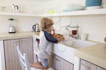 Young boy kneeling on a chair to wash dishes, full length