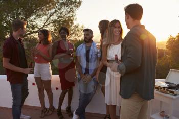 Young adult friends talk at a party on a rooftop at sunset