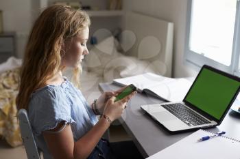 Teenage girl using smartphone at a desk in her bedroom