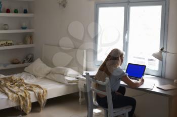 Teenage girl working with laptop at a desk in her bedroom