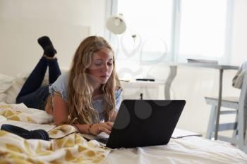 Teenage girl using laptop lying on her bed