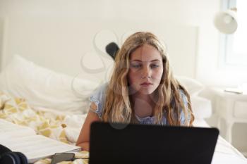 Teenage girl lying on bed working with laptop, close up