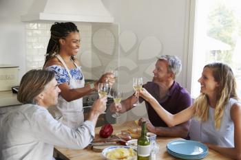 Two couples preparing dinner make a toast at kitchen table