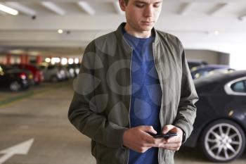 Man Sending Text Message On Mobile Phone In Car Park