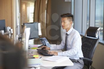 Young Businessman Sitting At Desk In Office Using Computer