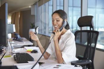 Businesswoman Making Phone Call Sitting At Desk In Office