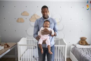 Portrait Of Father Holding Baby Daughter In Nursery