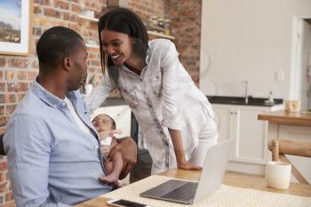 Father Working On Laptop Holds Newborn Son With Mother