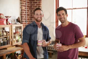 Two male friends hanging out in kitchen looking to camera