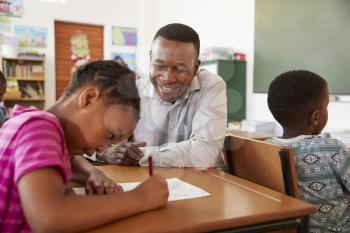 Black male teacher helping elementary school girl in class