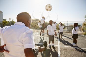 Boy kicking ball to classmates in elementary school playground