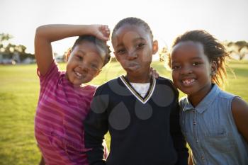 Three African elementary schoolgirls pose to camera in field