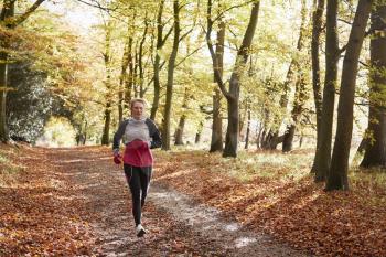 Mature Woman Running Through Autumn Woodland