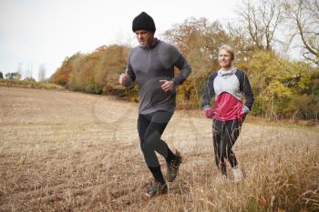 Mature Couple Running Around Autumn Field Together