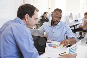 Two men discussing documents in a busy office