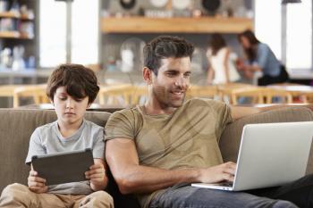 Father And Son Sitting On Lounge Sofa Using Digital Devices