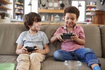 Two Boys Sitting On Sofa In Lounge Playing Video Game Together