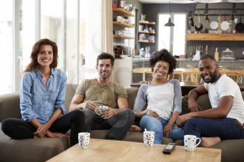 Portrait Of Couple Sitting On Sofa With Friends At Home Talking