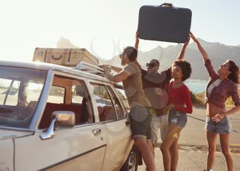 Friends Loading Luggage Onto Car Roof Rack Ready For Road Trip