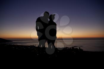 Couple standing and kissing by the sea at sunset on the beach