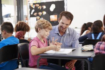 Teacher and young school boy looking at notebook in class