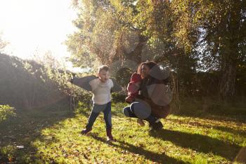 Mother And Children Playing With Autumn Leaves in Garden