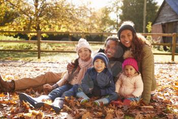 Portrait Of Family On Walk Sitting In Autumn Leaves