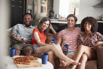 Young adult friends watching TV with food and drinks at home