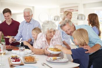 Multi-Generation Family And Friends Eating Food In Kitchen At Celebration Party