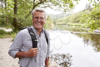 Portrait Of Senior Man Hiking Along Path By River In UK Lake District