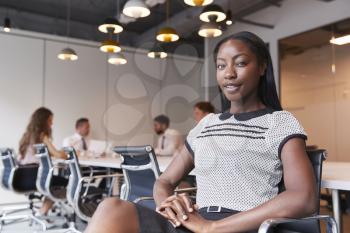 Portrait Of Businesswoman In Modern Boardroom With Colleagues Meeting Around Table In Background