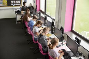 Line Of High School Students Working at Screens In Computer Class With Female Teacher In Background Shot From High Angle