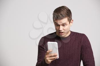 Portrait of a shocked young white man using a smartphone