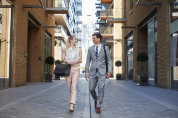 Businessman And Businesswoman Walk to Work Through City Street