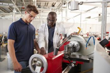 Engineer showing male apprentice how to operate machinery, close up