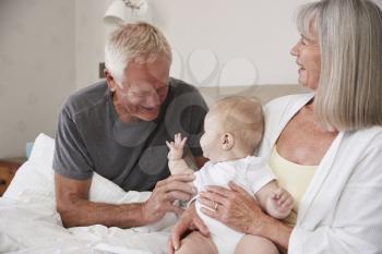 Grandparents Lying In Bed At Home Looking After Baby Grandson