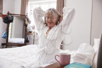 Senior Woman Waking Up And Stretching In Bedroom