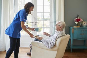 Nurse serving a cup of tea to a senior man at home