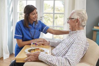 Nurse serving dinner to a senior man in an armchair at home