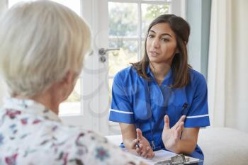 Senior woman talking to young care nurse on home visit