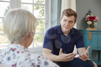 Senior woman talking with male care worker on home visit