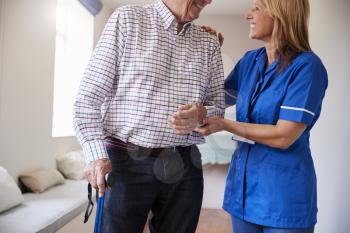 Nurse helping senior man walk using a walking stick