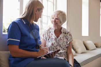 Senior woman sits with nurse making notes at retirement home