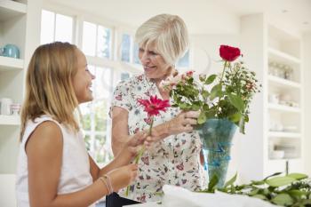 Senior woman arranging flowers with granddaughter at home