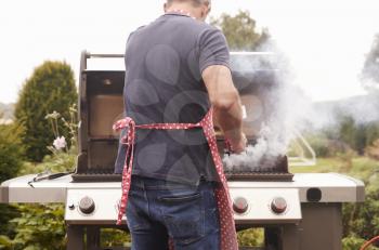 Middle aged man burning food on a barbecue, back view