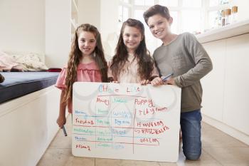 Portrait Of Children Making List Of Chores On Whiteboard At Home