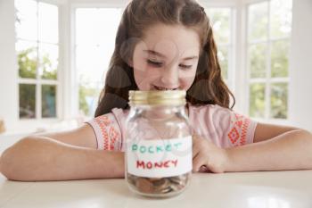 Girl Saving Pocket Money In Glass Jar At Home
