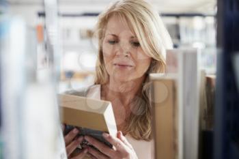 Mature Female Student Browsing Through Books In Library