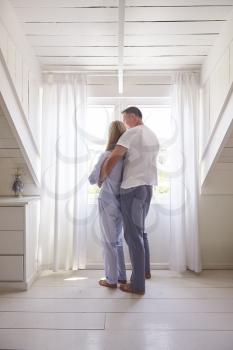 Rear View Of Affectionate Couple Standing By Bedroom Window
